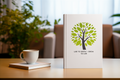 Book with a green tree design and text on a table with a cup and notebook.