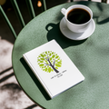 White notebook with green tree design and text on a green table with a cup of coffee.