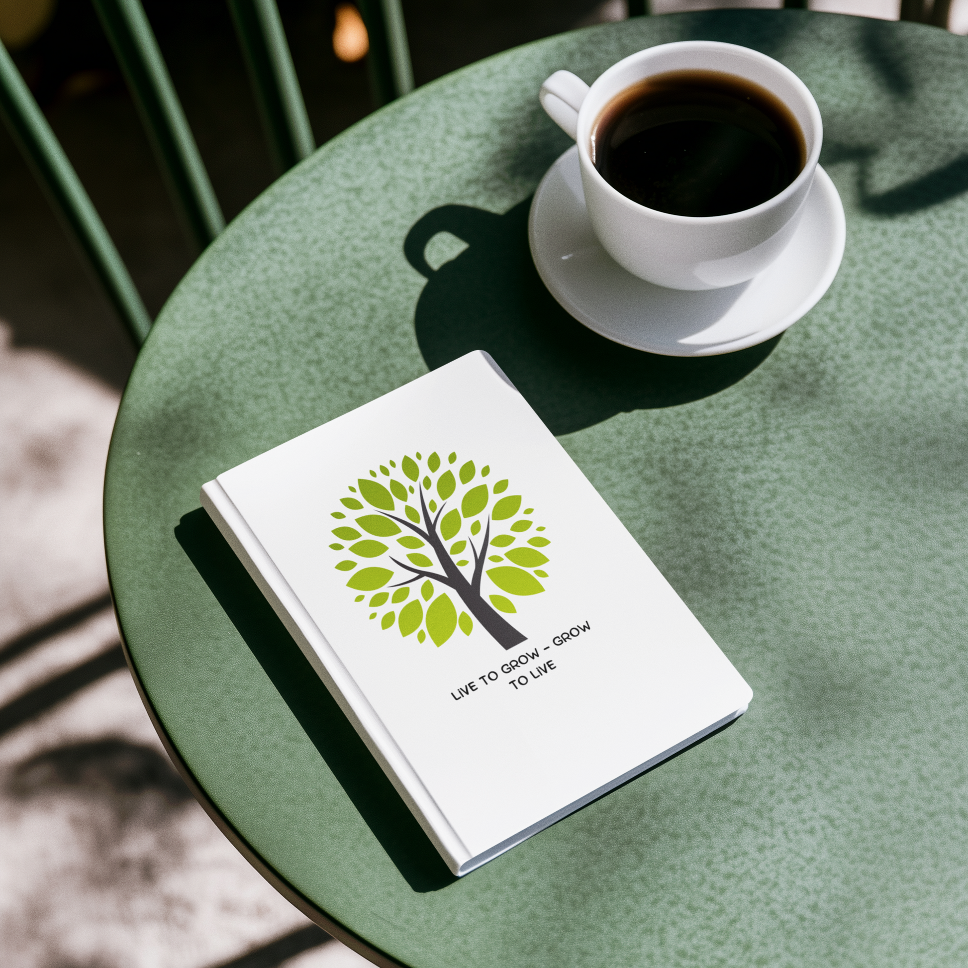 White notebook with green tree design and text on a green table with a cup of coffee.