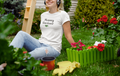 Woman in a garden wearing a 'Mummy Gardener' shirt, surrounded by plants and flowers.
