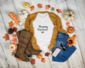 White t-shirt with 'Mommy Gardener' text, mustard sweater, blue jeans, brown boots, and fall decorations on a wooden floor.