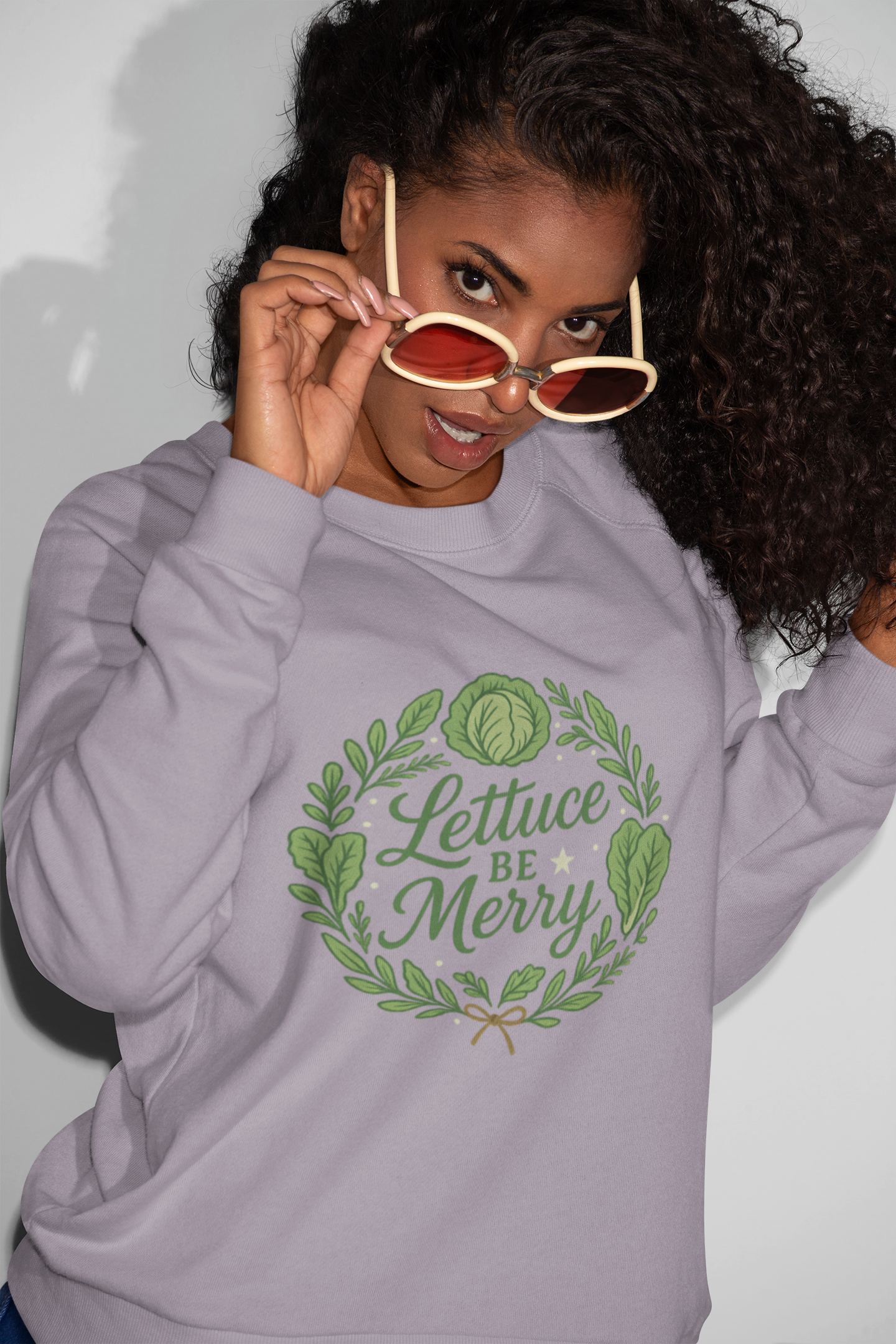 Person wearing a gray hoodie with 'Lettuce Be Merry' design, holding sunglasses.