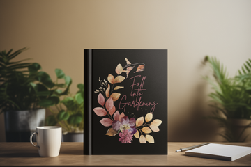 Black notebook with floral design and text on a wooden table with plants in the background