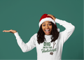 Person wearing a white sweatshirt with holiday text and a Santa hat on a green background