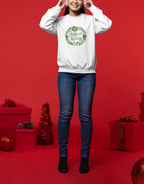 Person wearing a white sweatshirt with a green wreath design on a red background with Christmas decorations.