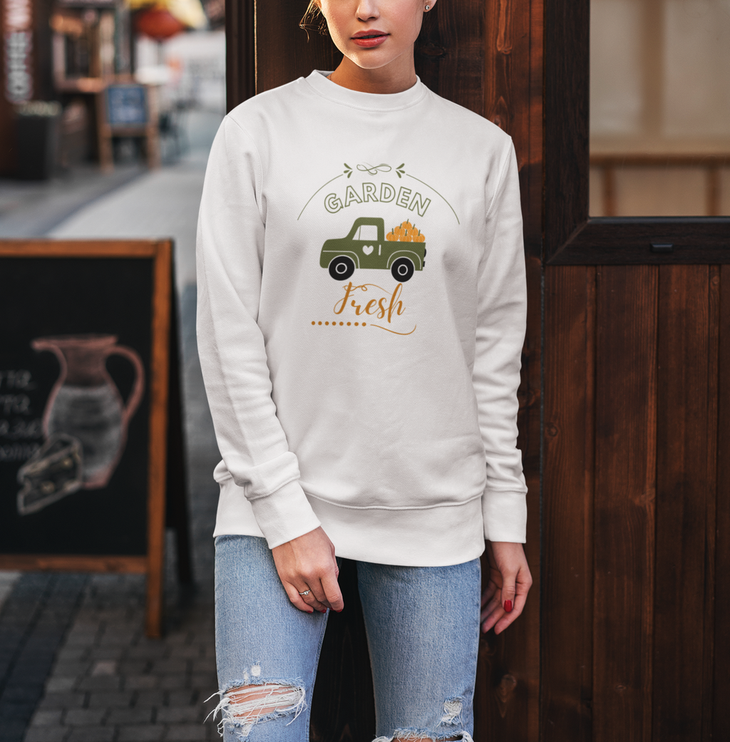Woman wearing a white sweatshirt with a graphic design standing in front of a wooden door.