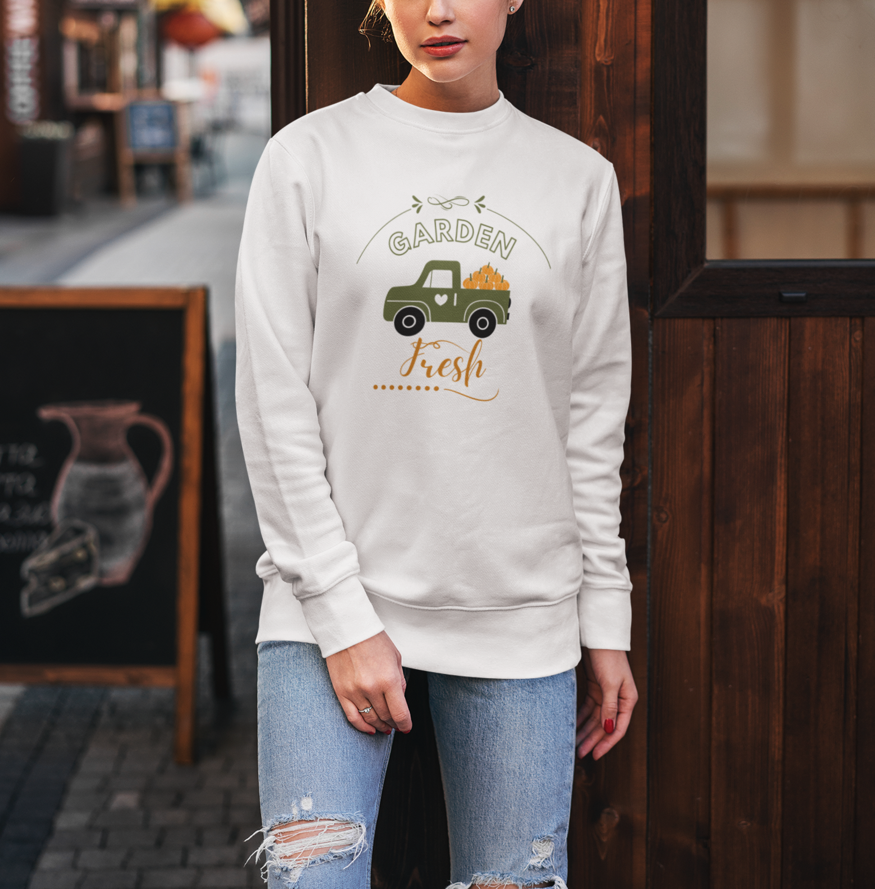 Woman wearing a white sweatshirt with a graphic design standing in front of a wooden door.