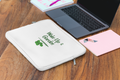 White pouch with 'Wake Up & Garden' text on a wooden surface with a laptop and notebook.