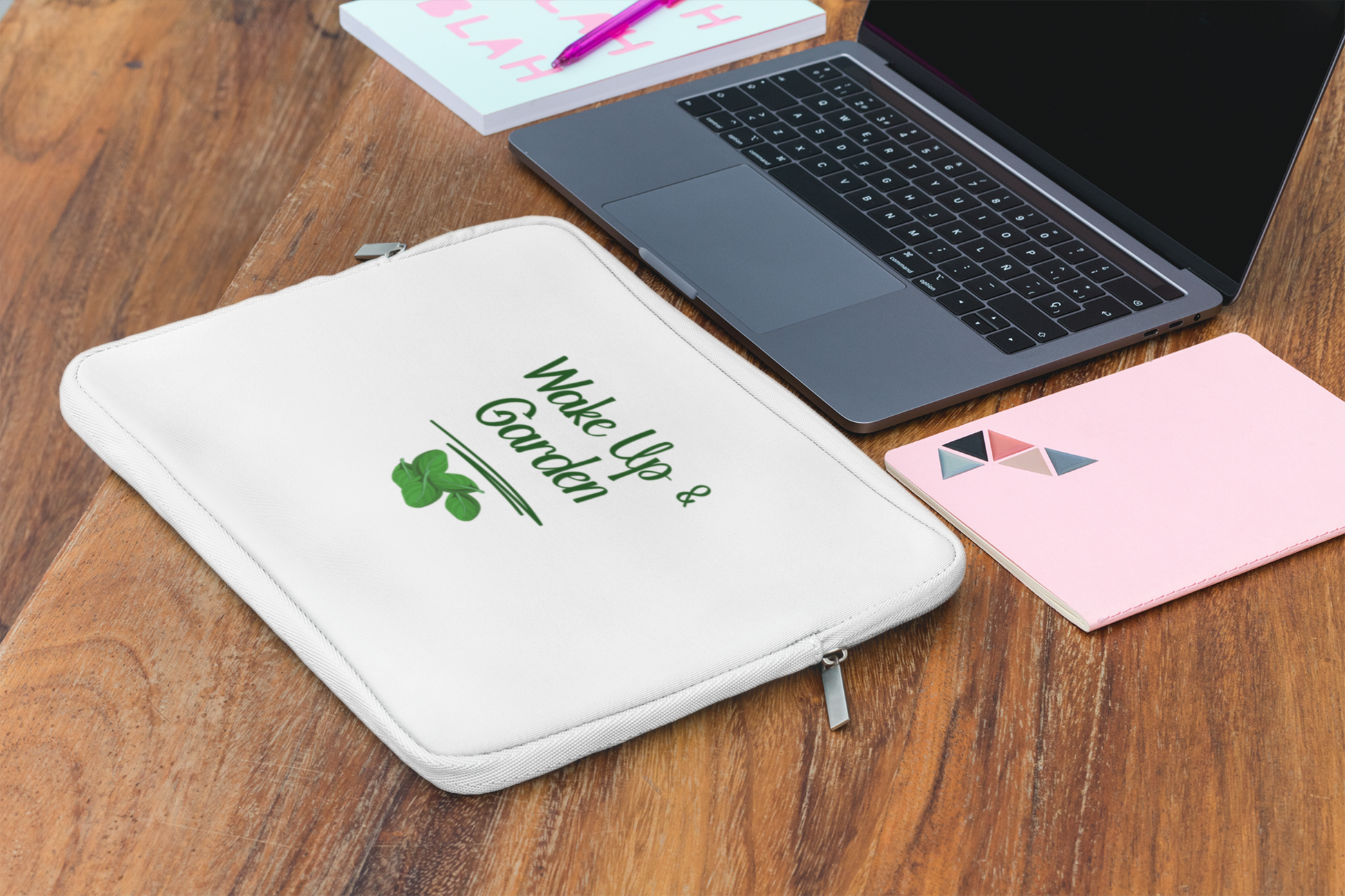 White pouch with 'Wake Up & Garden' text on a wooden surface with a laptop and notebook.