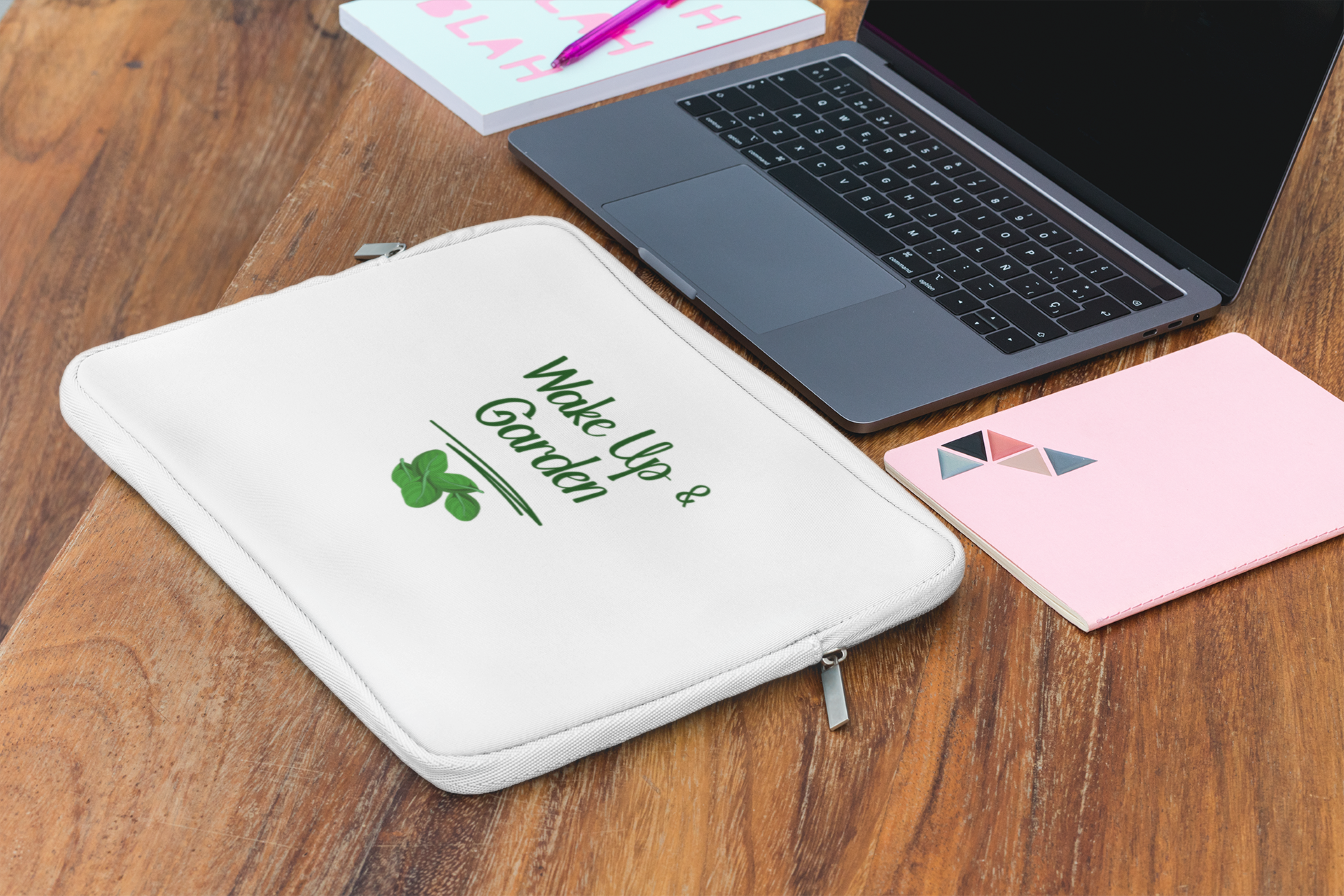 White pouch with 'Wake Up & Garden' text on a wooden surface with a laptop and notebook.