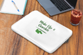 White laptop sleeve with 'Wake Up & Garden' text on a wooden desk with a laptop and glass of juice.
