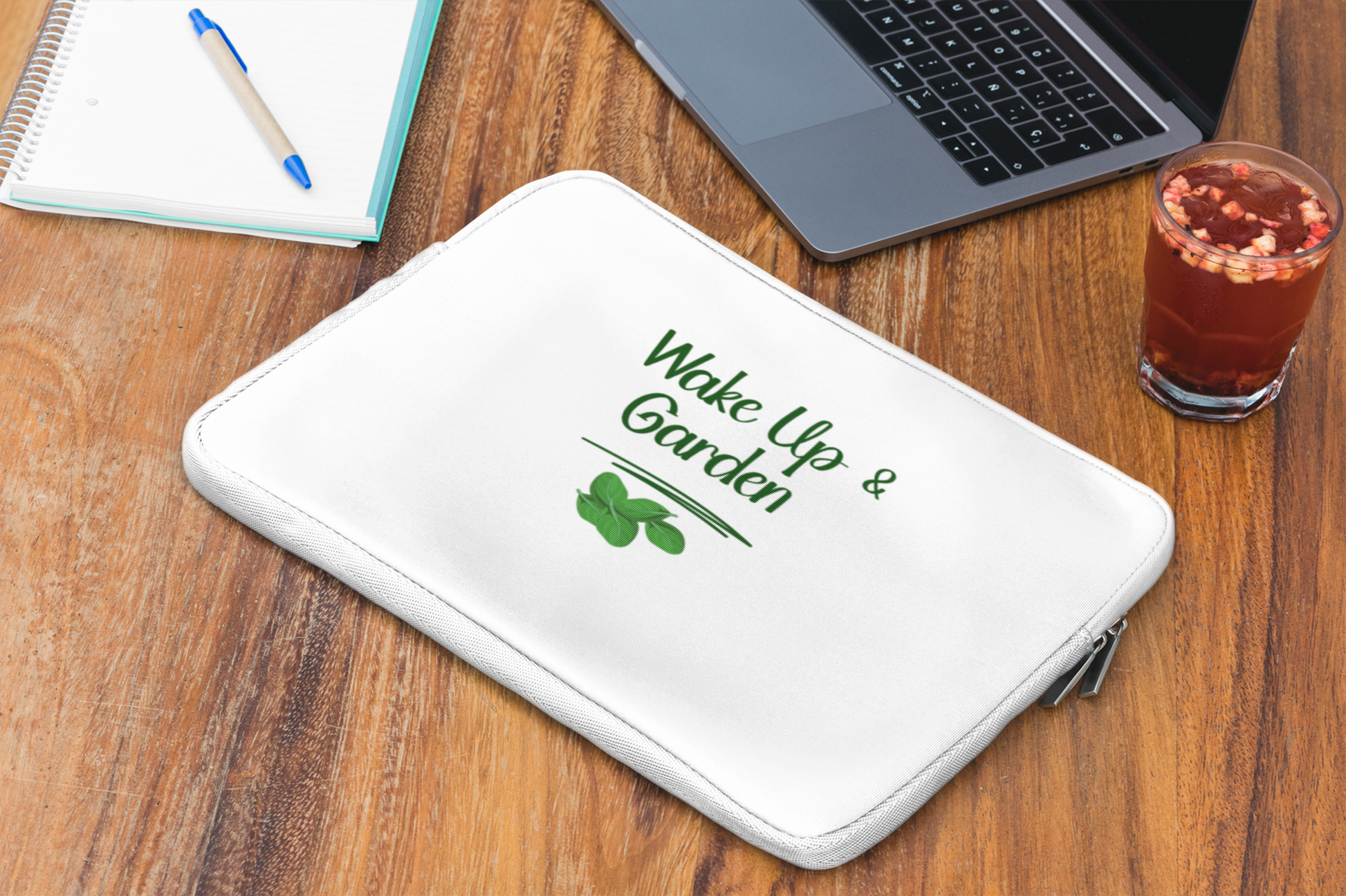 White laptop sleeve with 'Wake Up & Garden' text on a wooden desk with a laptop and glass of juice.