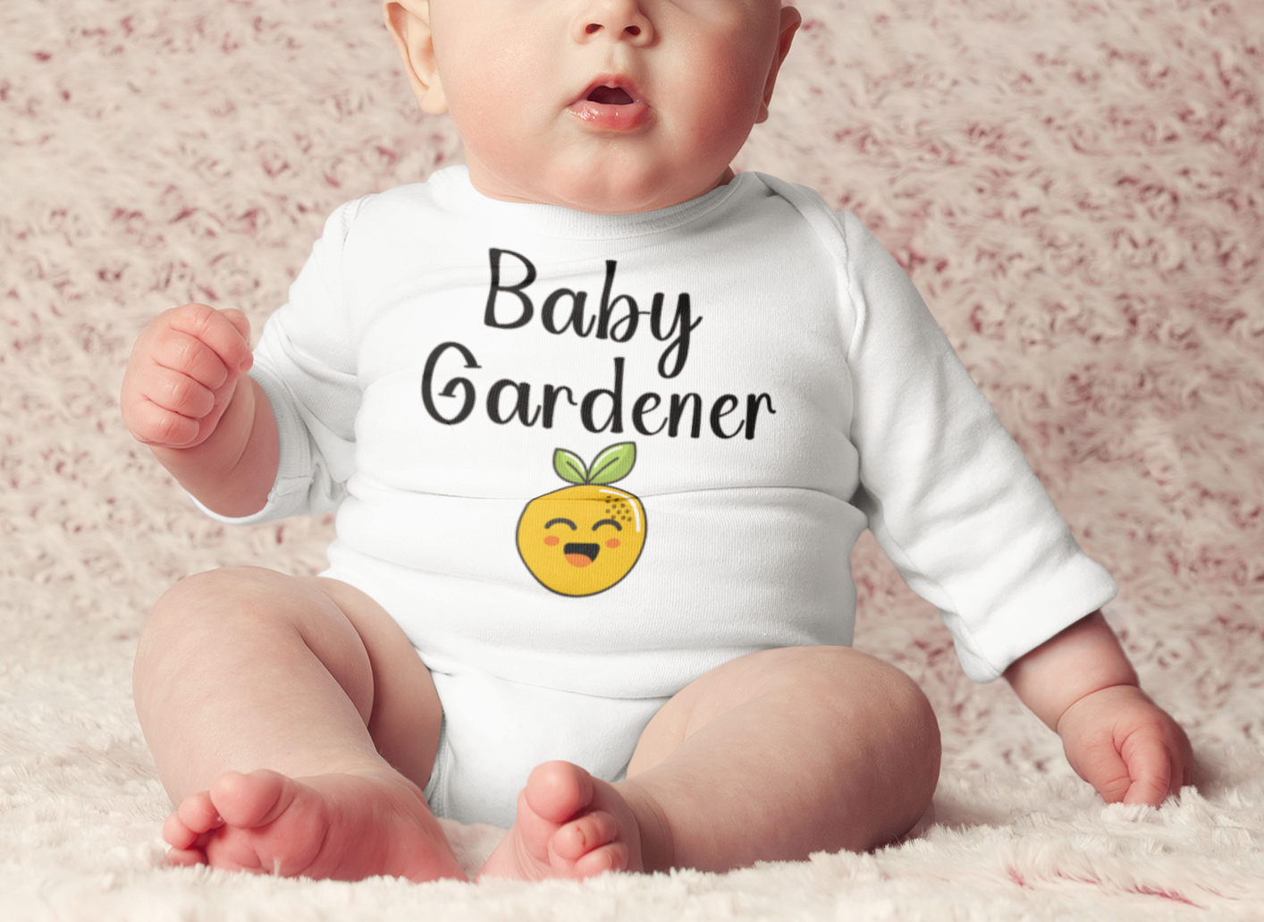 Baby wearing a 'Baby Gardener' onesie with a smiling sun emoji on a soft pink background.