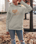 Woman wearing a light gray hoodie with a tree design outdoors in autumn.