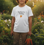Child wearing a 'Gardener in Training' t-shirt holding carrots in a garden.
