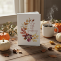Book titled 'Fall into Gardening' on a wooden table with pumpkins and a steaming cup of coffee.