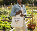 Person holding a tote bag with 'Gardener For Life' text in a garden setting