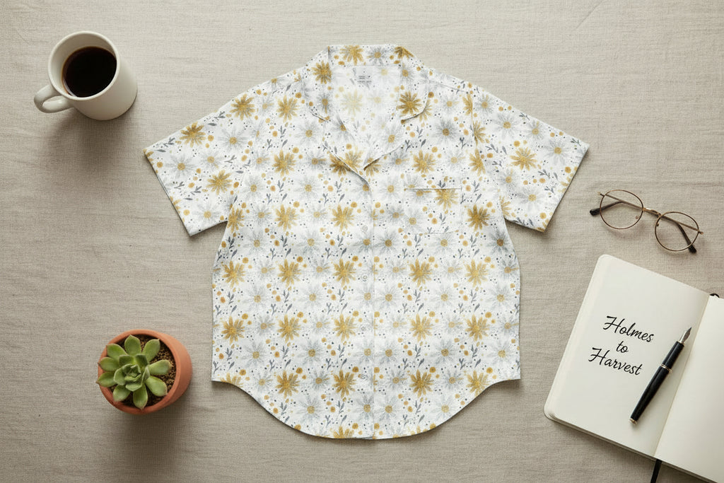 Floral patterned shirt on a wooden surface with a cup, plant, notebook, and glasses.