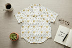 Floral patterned shirt on a wooden surface with a cup, plant, notebook, and glasses.