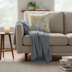 Beige sofa with a floral pillow and gray blanket in a living room setting.