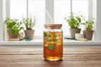 Jar of iced tea with a straw on a wooden surface, plants in the background