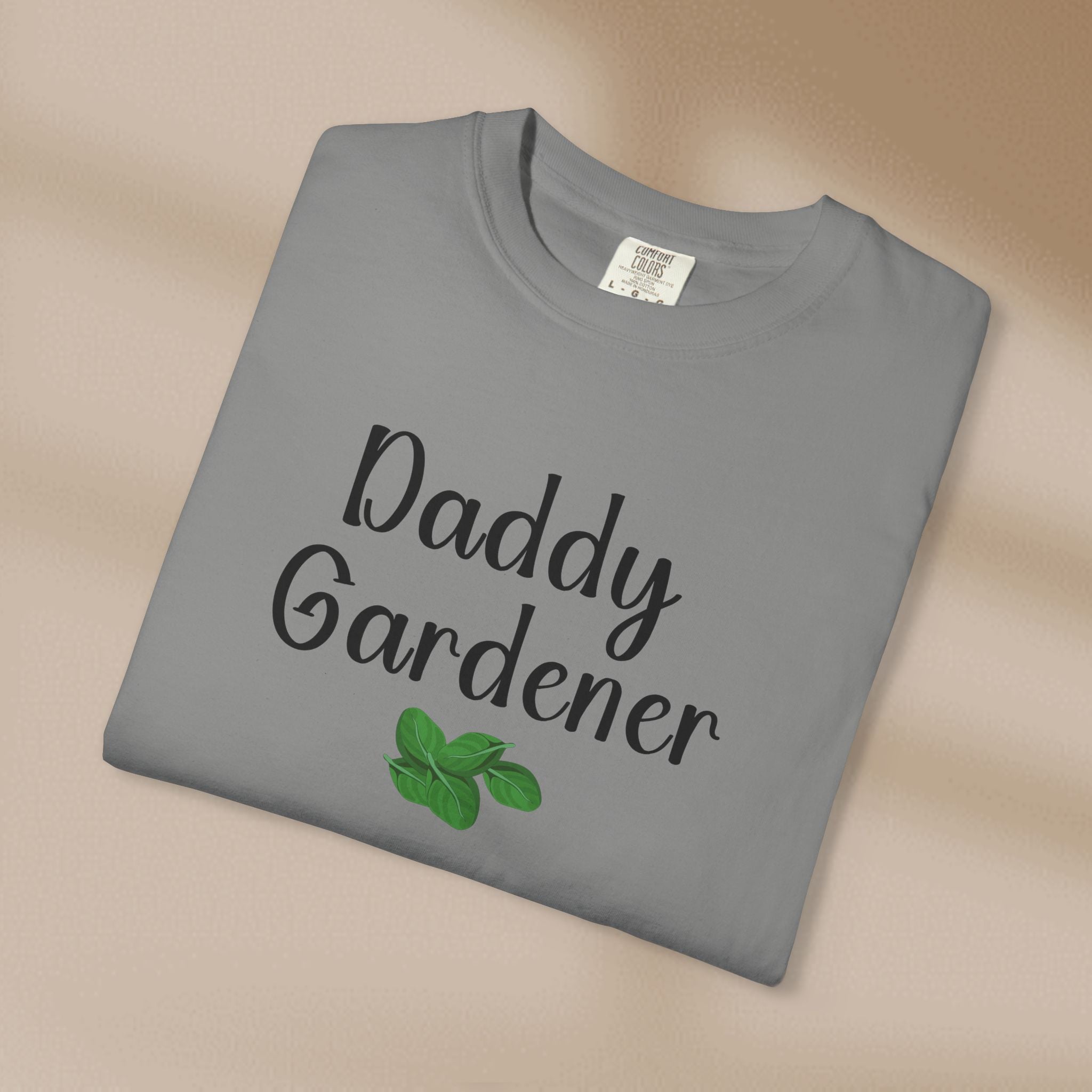 Folded gray t-shirt with 'Daddy Gardener' text and green leaves on a beige background