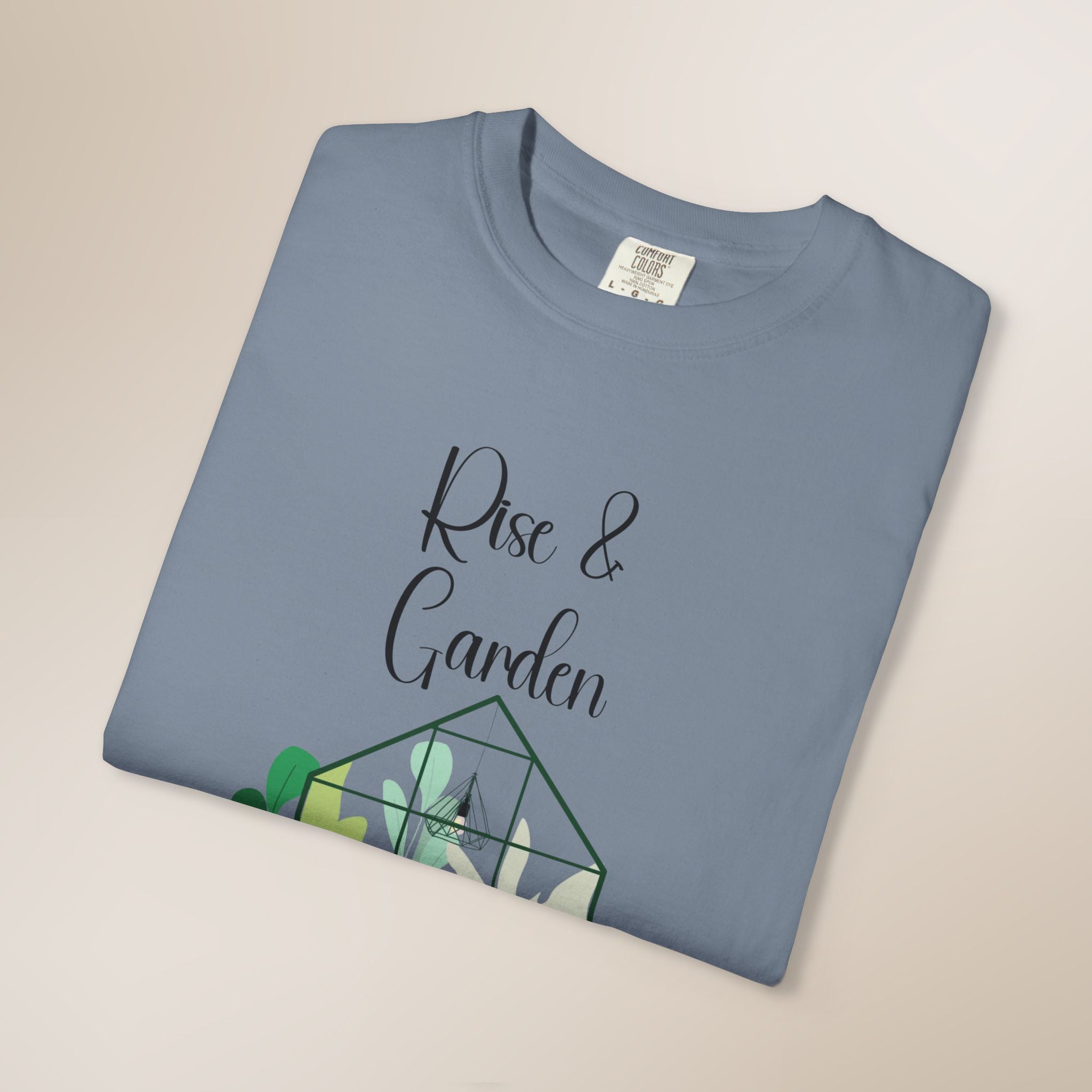 Folded blue t-shirt with 'Rise & Garden' text and terrarium design on a beige background