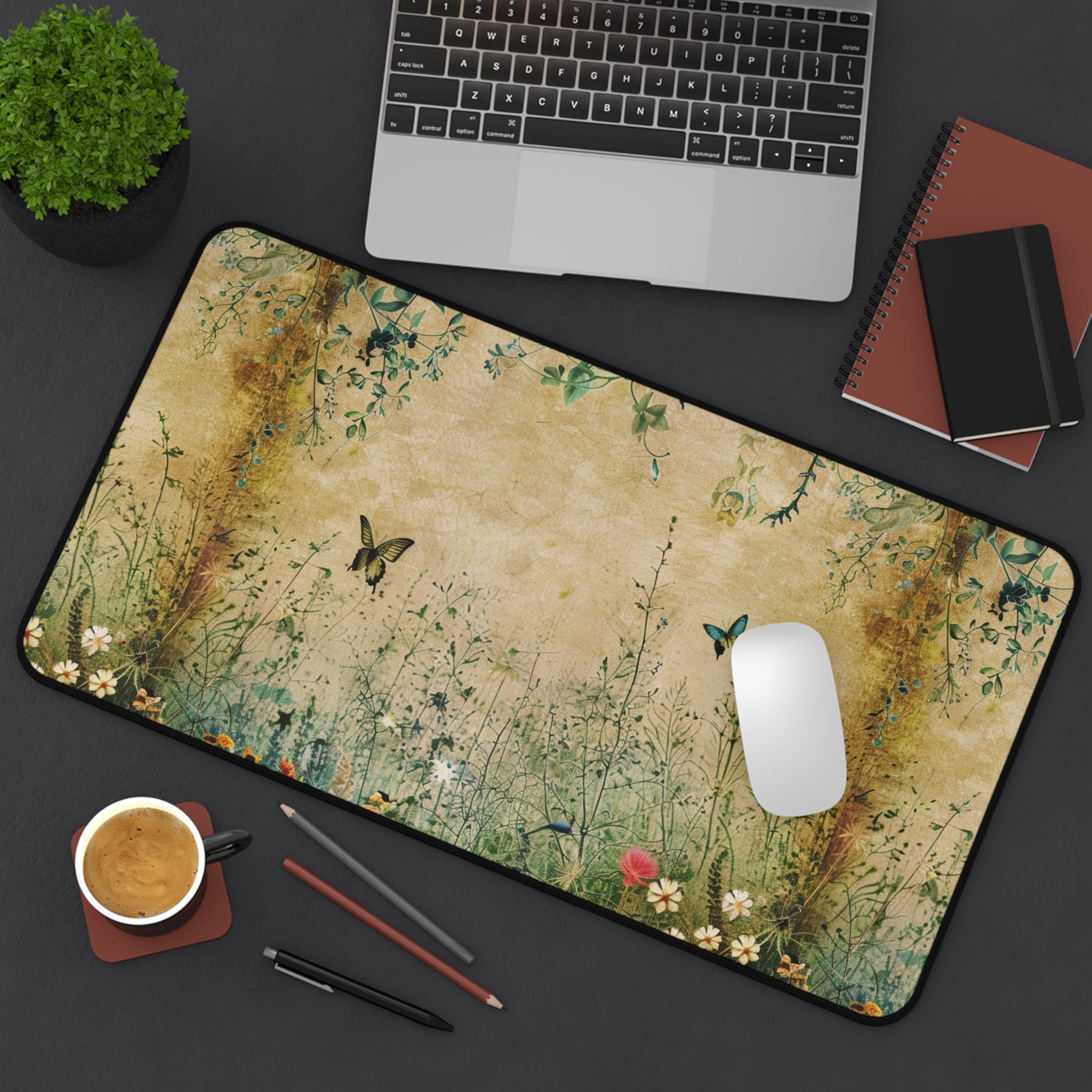 Desk setup with a decorative mouse pad featuring nature-themed design, laptop, notebook, and coffee cup.
