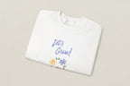 White shirt with 'Let's Grow!' text and floral designs on a white background