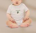Baby wearing a white onesie with green text and leaf design on a beige background