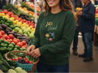 Woman wearing a green sweatshirt with 'Let's Grow!' text at an outdoor market.