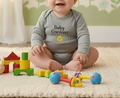 Baby in a 'Baby Gardener' onesie surrounded by toys on a carpeted floor.