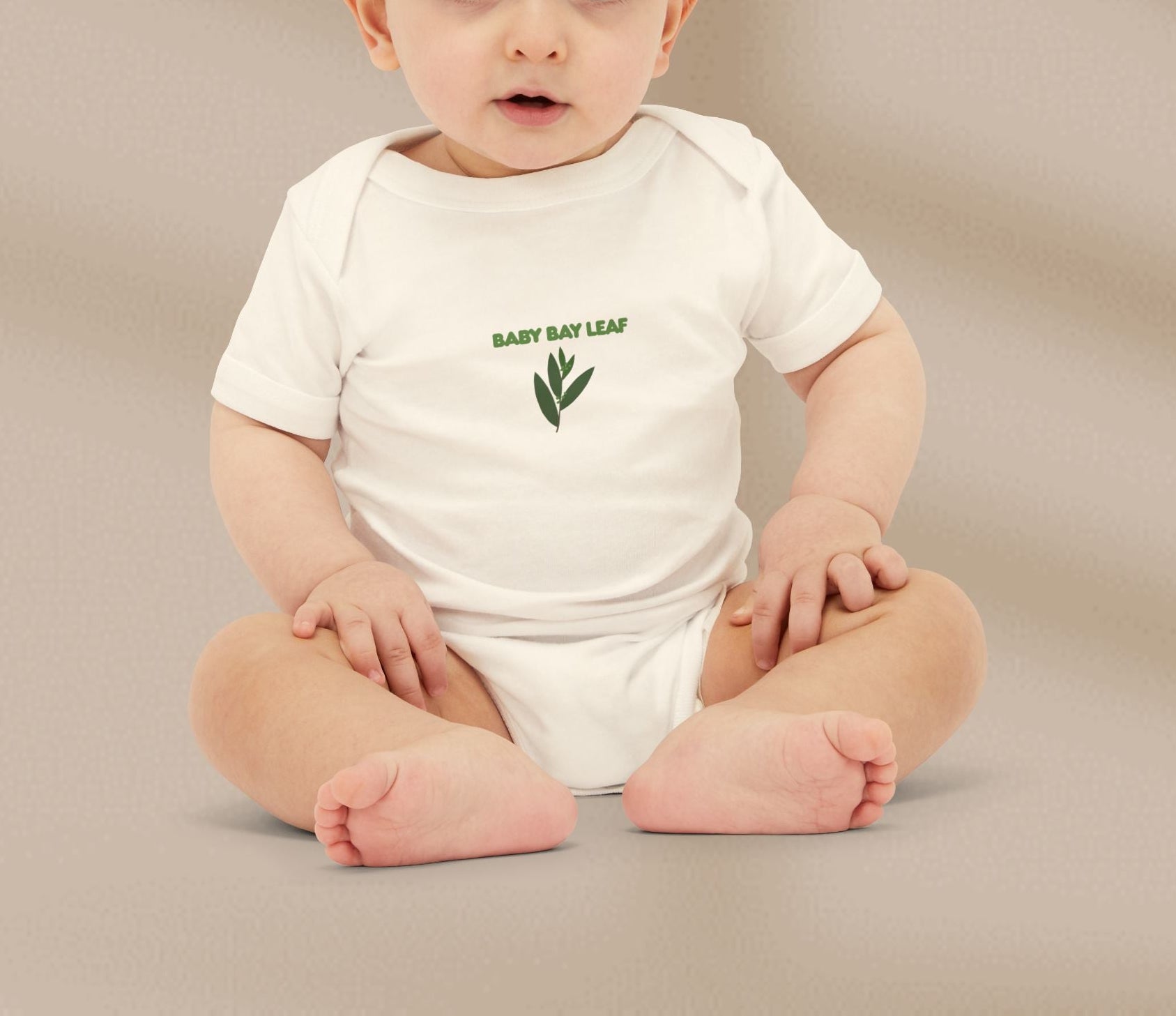 Baby wearing a white onesie with 'Baby Bay Leaf' text and leaf graphic on a beige background