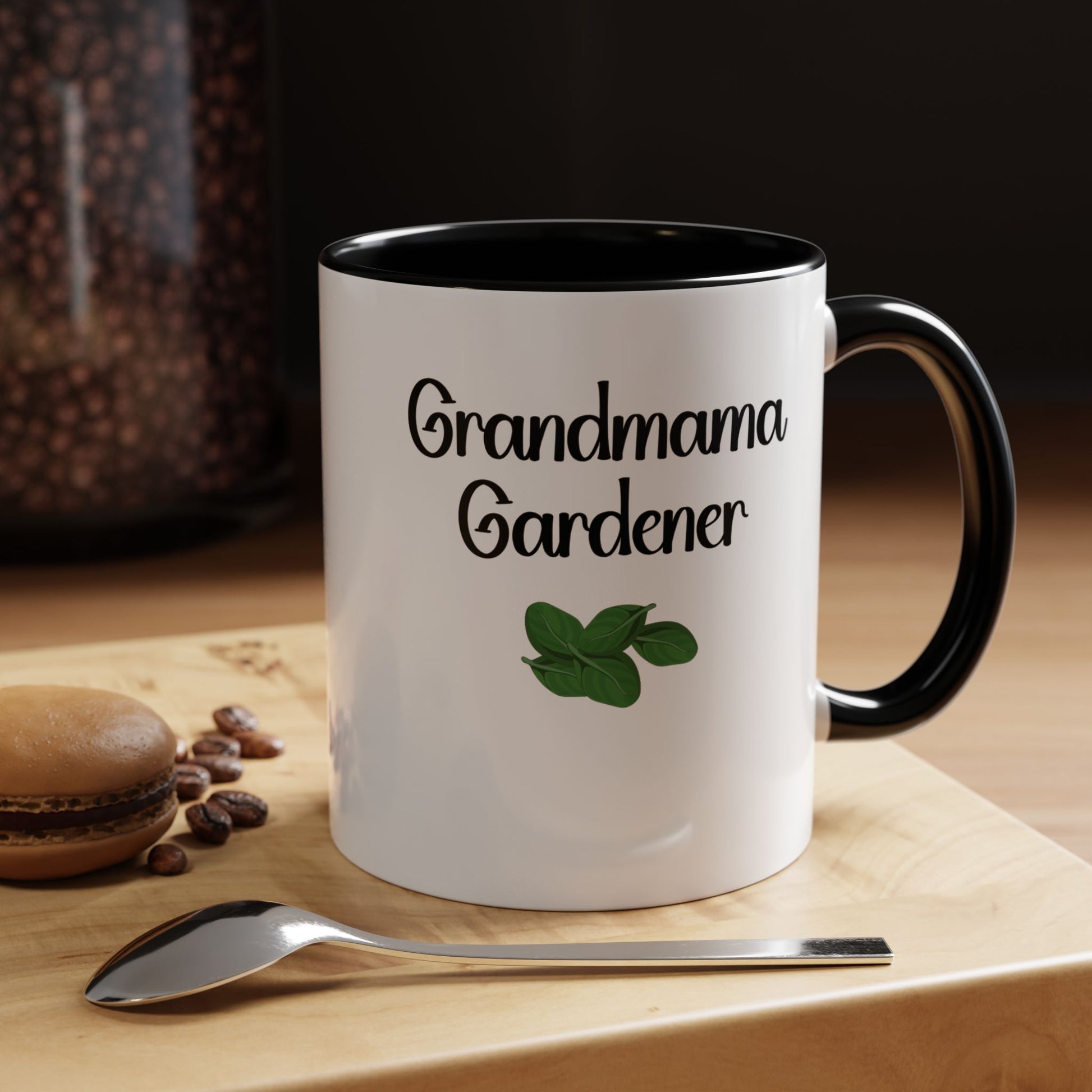 White mug with 'Grandmama Gardener' text and green leaf design on a wooden surface with coffee beans and a spoon.