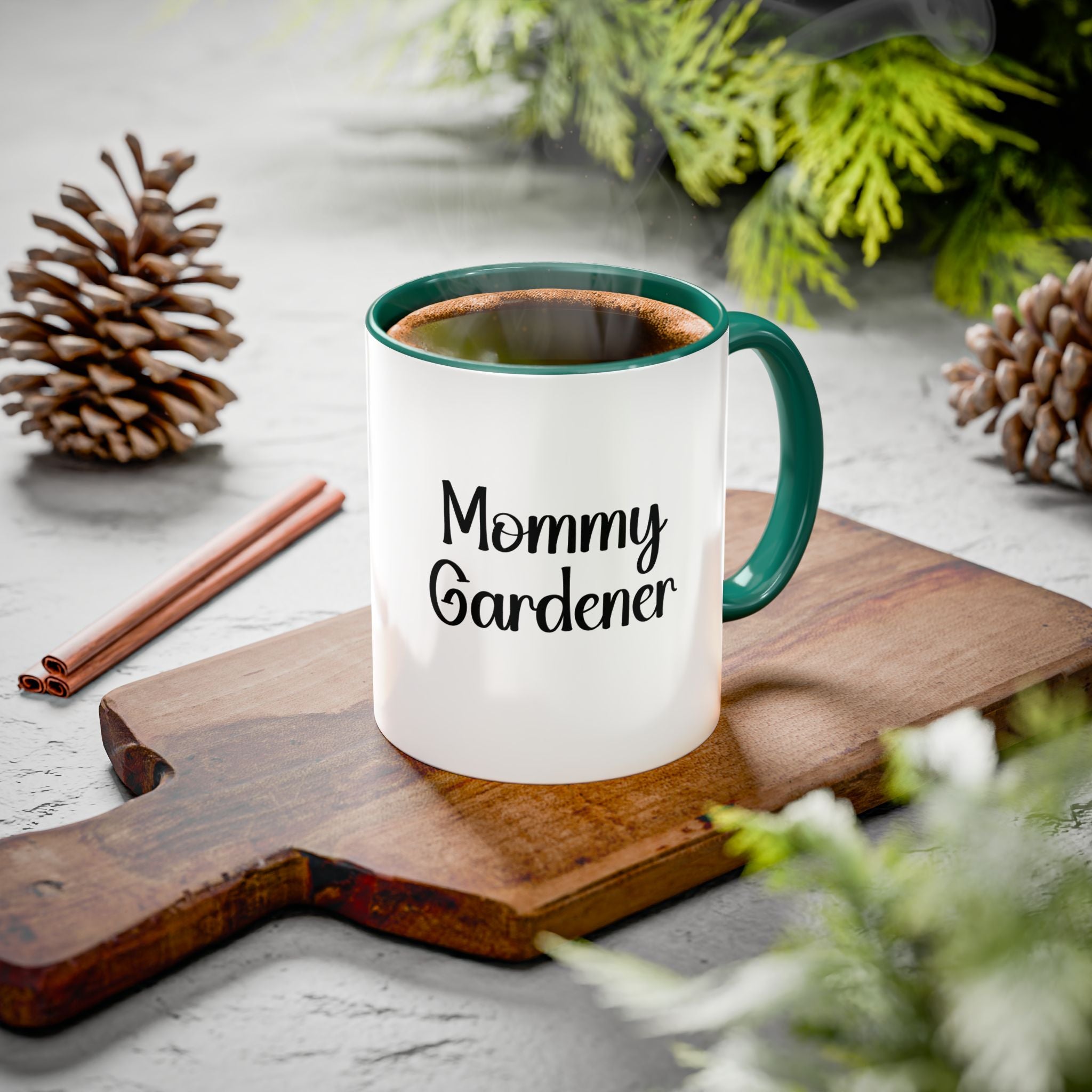 Mug with 'Mommy Gardener' text on a wooden board with pinecones and cinnamon sticks.