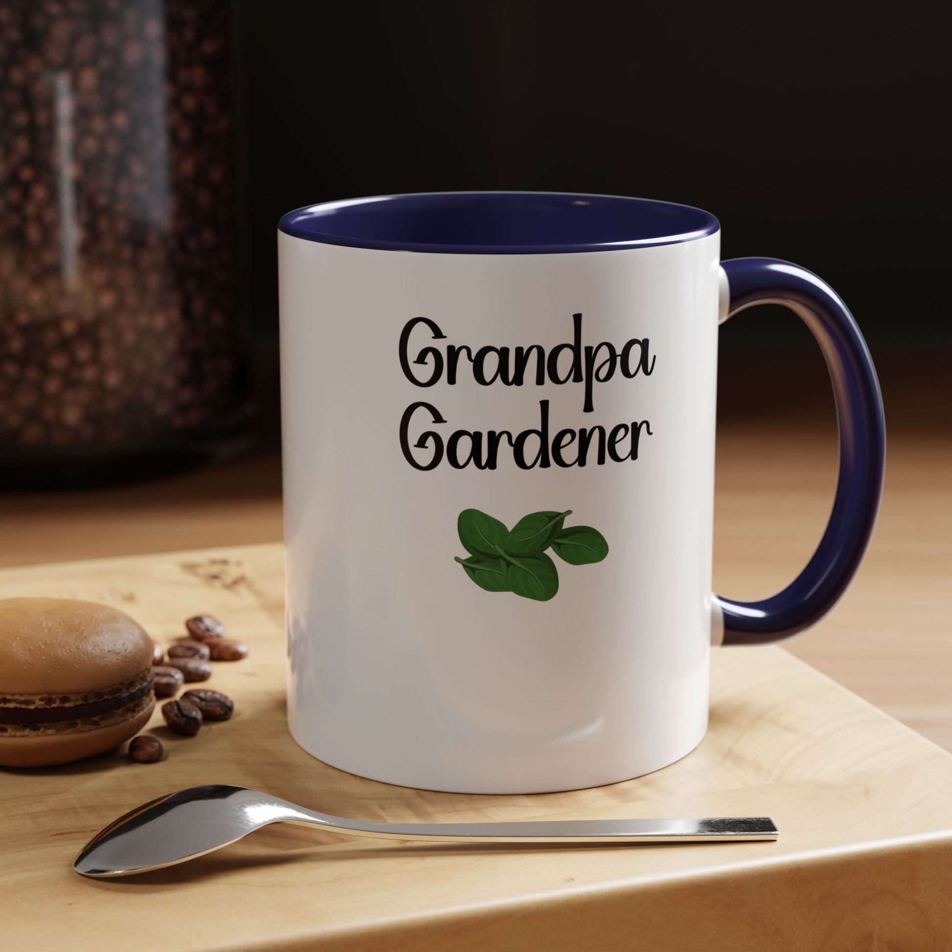 Mug with 'Grandpa Gardener' text and leaf design on a wooden surface with coffee beans and a spoon.