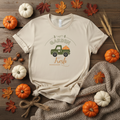 Beige t-shirt with a green truck graphic and 'Garden Fresh' text on a wooden surface with pumpkins and leaves.