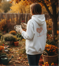 Person wearing a white hoodie with a tree design in an autumn garden.