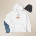 White hoodie with a tree graphic and text, paired with a black beanie and blue jeans on a beige background