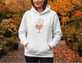 Person wearing a white hoodie with 'Fall into Gardening' text and tree design in an autumn garden setting.