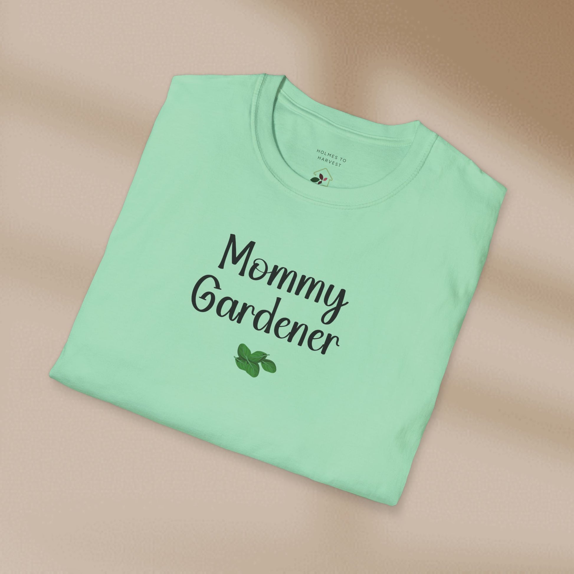Folded light green t-shirt with 'Mommy Gardener' text on a beige background