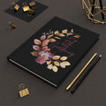 Black notebook with floral design and text on a dark surface with stationery items.
