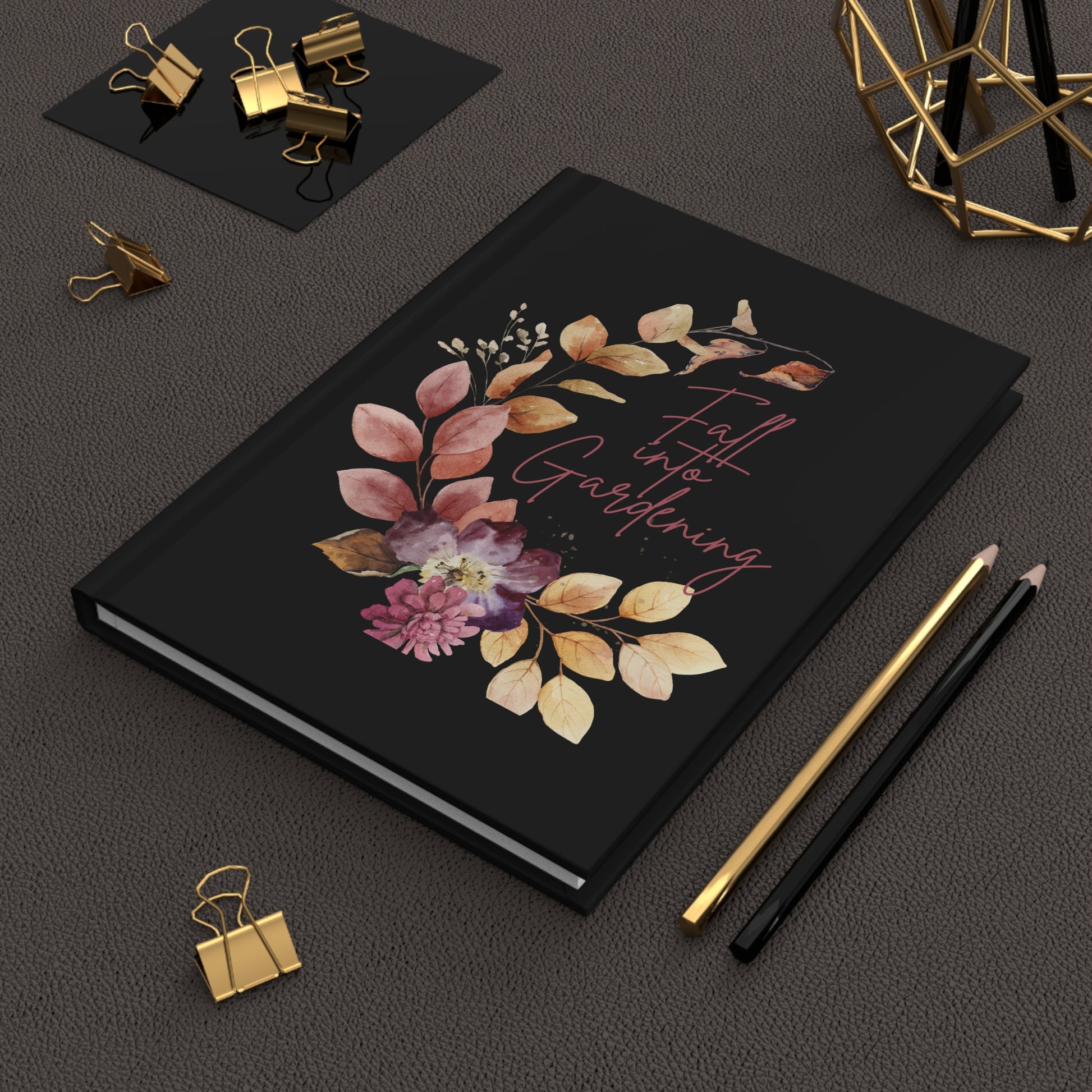 Black notebook with floral design and text on a dark surface with stationery items.