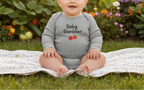 Baby wearing a 'Baby Gardener' onesie sitting on a blanket outdoors.