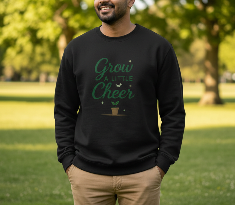Man wearing a black sweatshirt with 'Grow a Little Cheer' text and plant graphic in a park.