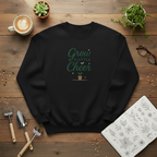 Black sweatshirt with 'Grow a Little Cheer' text on a wooden surface with plants and a cup of coffee.