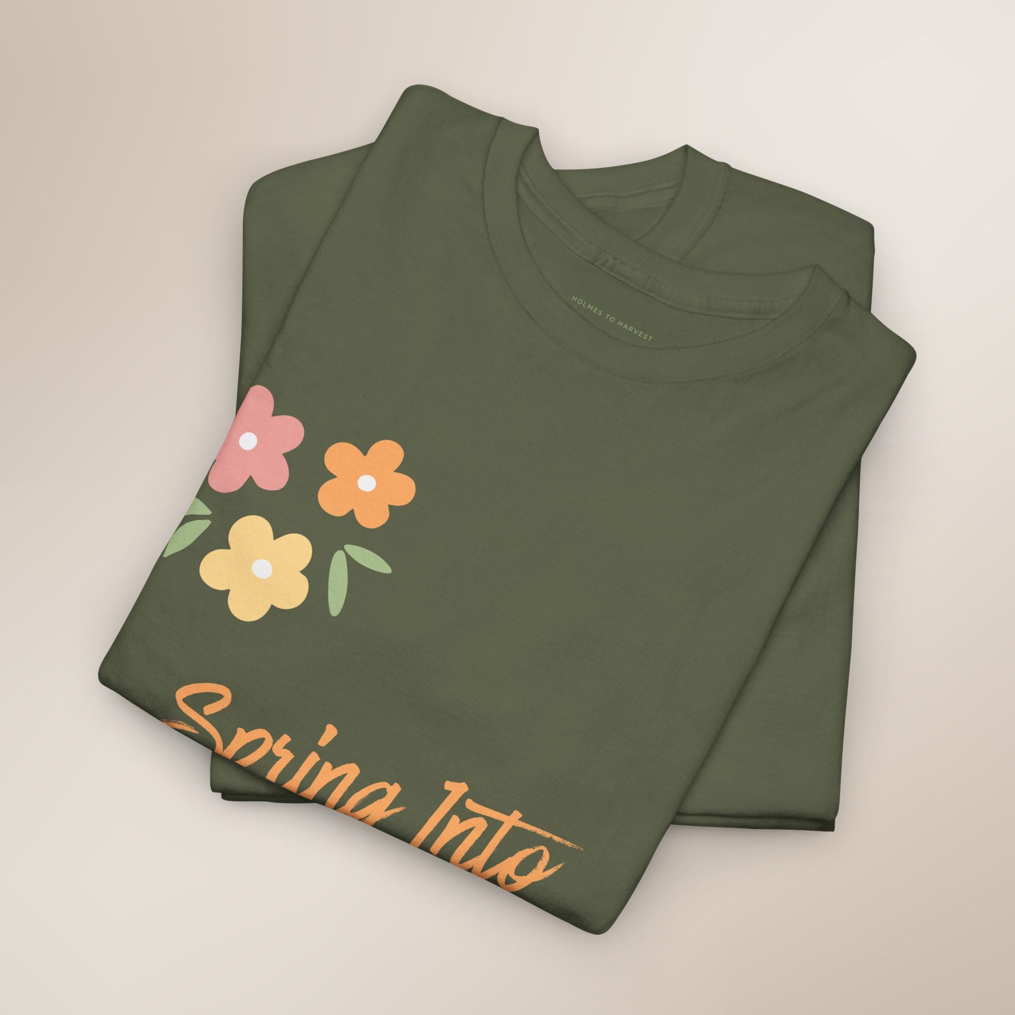 Folded green t-shirt with floral design and 'Spring Into' text on a beige background