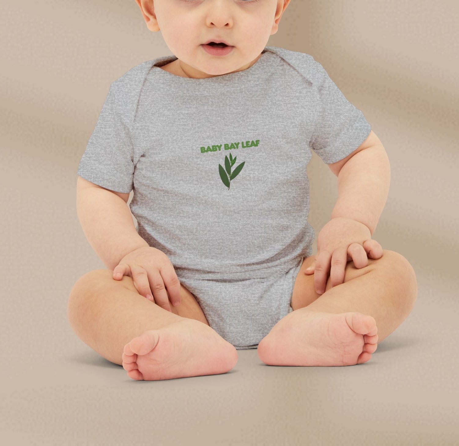 Baby wearing a gray onesie with 'Baby Bay Leaf' text and logo on a beige background
