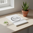 White book with 'The Garden' logo on a wooden surface next to a potted plant.
