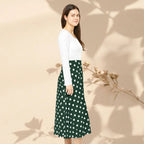 Woman wearing a white top and green polka dot skirt against a beige background